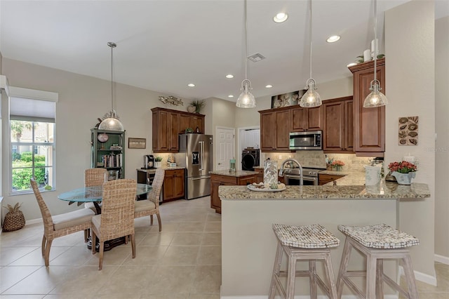 kitchen featuring washer / dryer, appliances with stainless steel finishes, kitchen peninsula, decorative light fixtures, and a breakfast bar