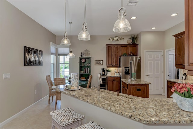 kitchen featuring light stone counters, high end fridge, a kitchen island, and hanging light fixtures