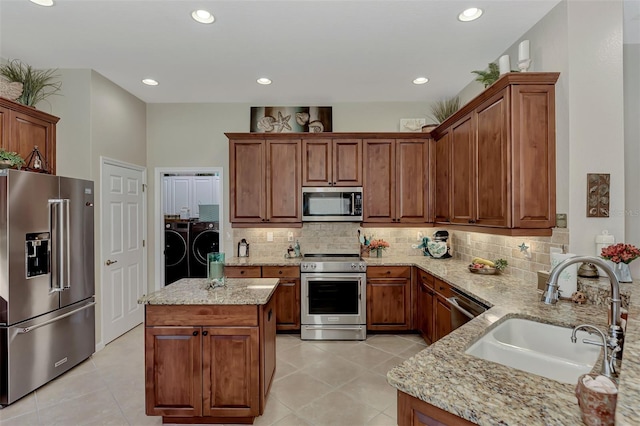 kitchen with washing machine and clothes dryer, light tile patterned flooring, light stone countertops, appliances with stainless steel finishes, and a sink