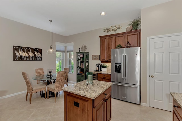 kitchen featuring hanging light fixtures, stainless steel fridge, light stone countertops, a center island, and light tile patterned floors