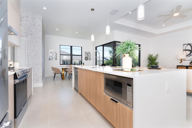 kitchen with an island with sink, appliances with stainless steel finishes, light tile patterned floors, pendant lighting, and sink