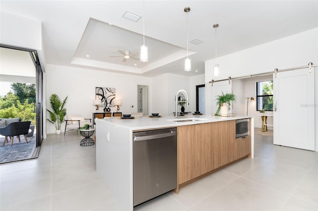 kitchen featuring a spacious island, a barn door, a tray ceiling, dishwasher, and sink