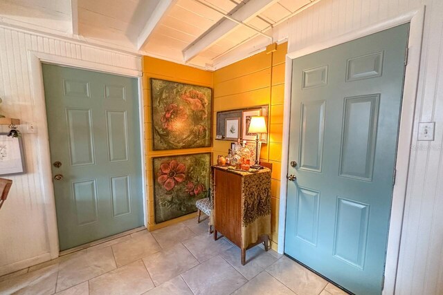 tiled entryway featuring beam ceiling and wood walls