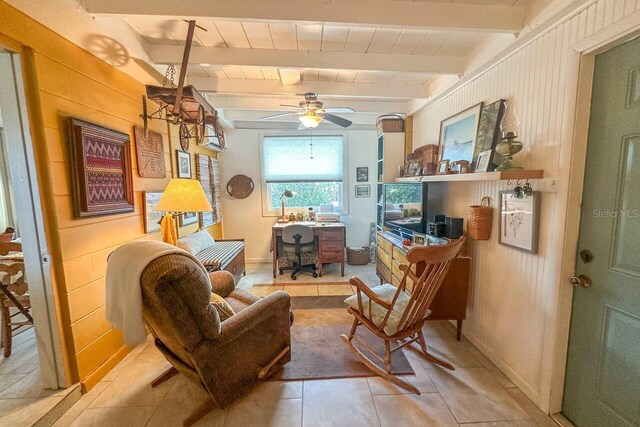 sitting room featuring ceiling fan, beamed ceiling, light tile patterned flooring, and wooden walls