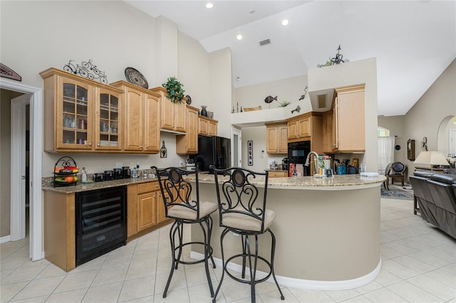 kitchen with wine cooler, a breakfast bar area, high vaulted ceiling, black appliances, and light stone counters