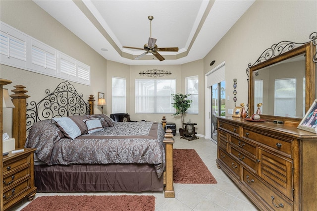 tiled bedroom with ceiling fan and a tray ceiling