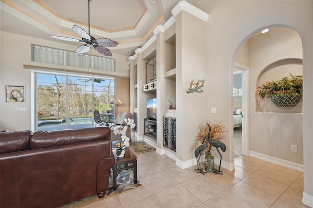 tiled living room with ceiling fan, a raised ceiling, built in features, and ornamental molding