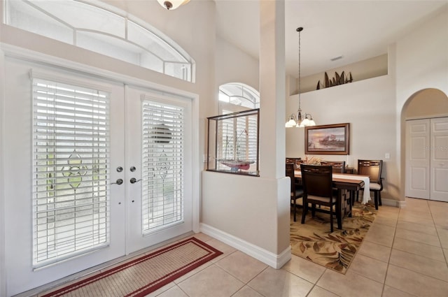 foyer entrance featuring a chandelier, french doors, a towering ceiling, and light tile patterned flooring