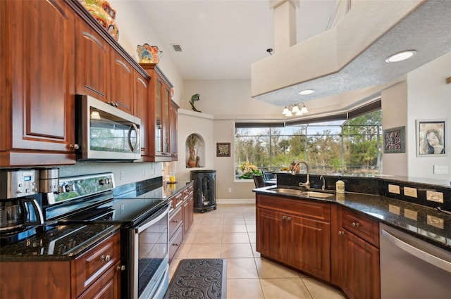 kitchen featuring sink, dark stone counters, a textured ceiling, light tile patterned floors, and appliances with stainless steel finishes