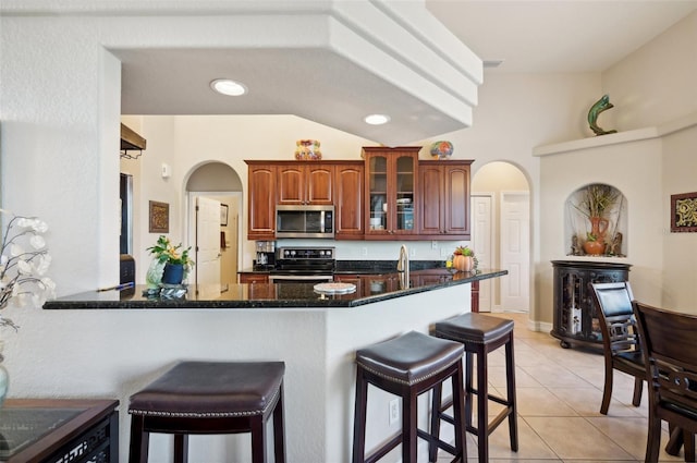 kitchen featuring vaulted ceiling, light tile patterned floors, a kitchen bar, kitchen peninsula, and stainless steel appliances