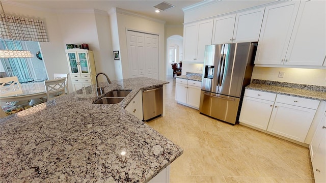 kitchen with appliances with stainless steel finishes, an island with sink, sink, white cabinets, and light stone counters