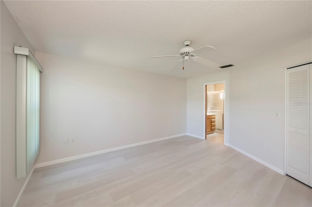 unfurnished bedroom featuring connected bathroom, a closet, light wood-type flooring, a textured ceiling, and ceiling fan