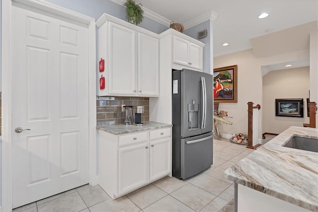 kitchen with light stone countertops, backsplash, stainless steel fridge, white cabinets, and ornamental molding