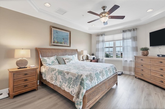 bedroom featuring crown molding, a tray ceiling, light wood-type flooring, and ceiling fan