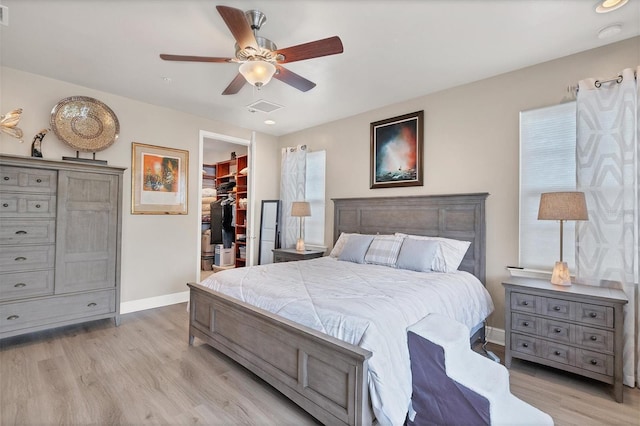 bedroom featuring a walk in closet, a closet, light wood-type flooring, and ceiling fan