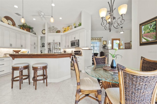 tiled dining space featuring high vaulted ceiling and ceiling fan with notable chandelier