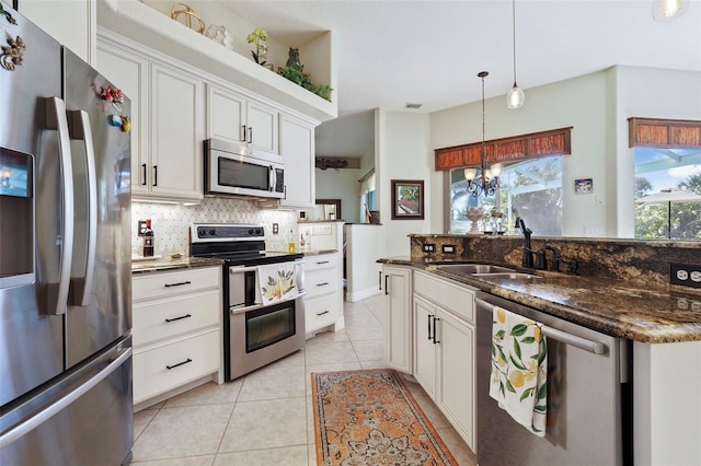 kitchen with hanging light fixtures, white cabinetry, dark stone countertops, sink, and stainless steel appliances