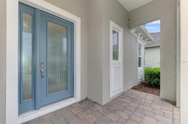 view of exterior entry with stucco siding and a patio area