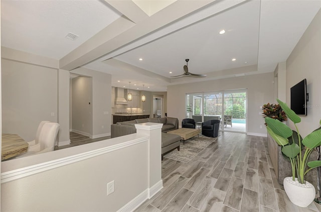 living room with a ceiling fan, visible vents, a raised ceiling, baseboards, and light wood finished floors