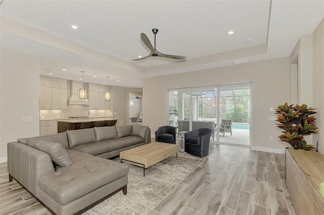 living area with light wood-style floors, a raised ceiling, a ceiling fan, and recessed lighting