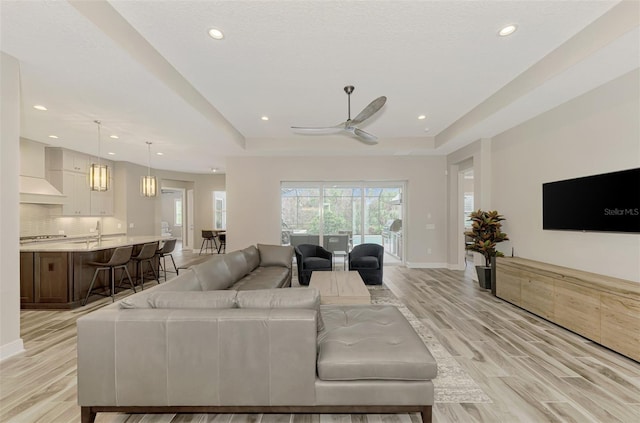 living room with ceiling fan, light wood-type flooring, and a tray ceiling