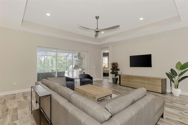 living room with ceiling fan, light wood-type flooring, and a tray ceiling