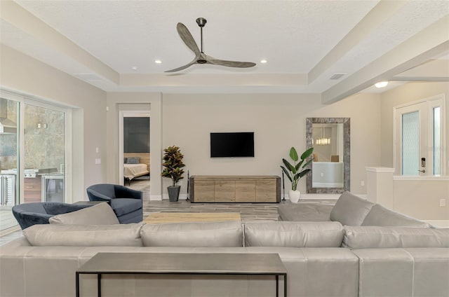 living room with ceiling fan, a textured ceiling, and a tray ceiling