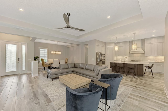 living room featuring light hardwood / wood-style flooring, ceiling fan, sink, and a tray ceiling