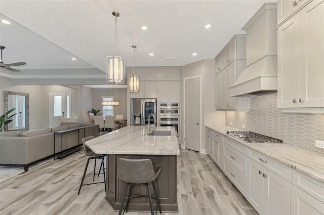 kitchen featuring decorative backsplash, light stone countertops, light wood-style floors, premium range hood, and stainless steel appliances