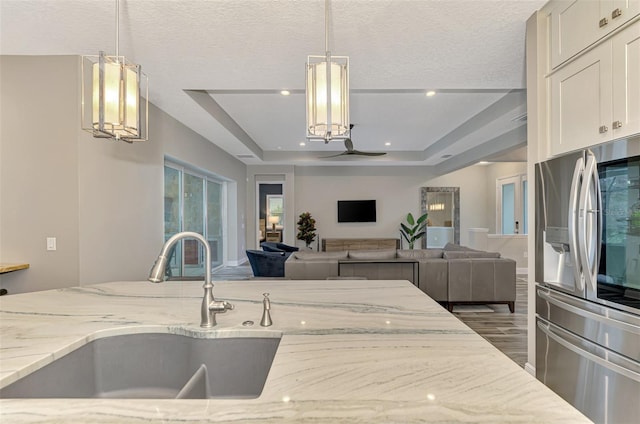 kitchen featuring light stone counters, a raised ceiling, stainless steel refrigerator with ice dispenser, hanging light fixtures, and hardwood / wood-style flooring