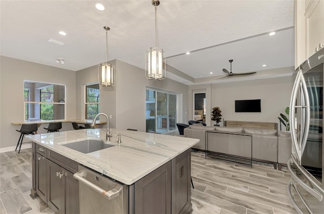 kitchen featuring light stone countertops, hanging light fixtures, a sink, stainless steel appliances, and a ceiling fan