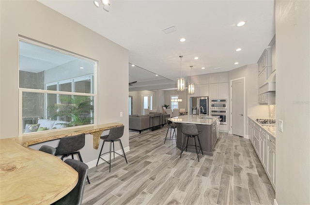 kitchen featuring a wealth of natural light, hanging light fixtures, a center island with sink, and a breakfast bar