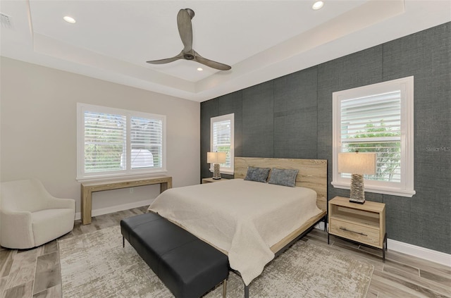 bedroom featuring hardwood / wood-style floors, ceiling fan, multiple windows, and a raised ceiling