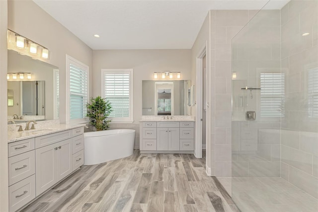 full bathroom with a freestanding tub, wood finished floors, two vanities, a sink, and a stall shower