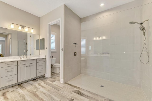 bathroom with hardwood / wood-style flooring, vanity, toilet, and tiled shower