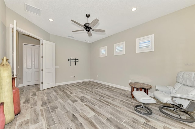 living area with a textured ceiling, light wood-type flooring, and ceiling fan