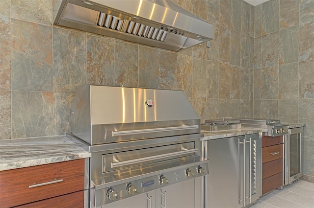 kitchen with tile walls, light stone counters, light tile patterned floors, and wall chimney range hood