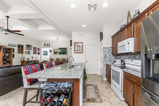 kitchen with sink, light stone counters, a kitchen bar, an island with sink, and white appliances