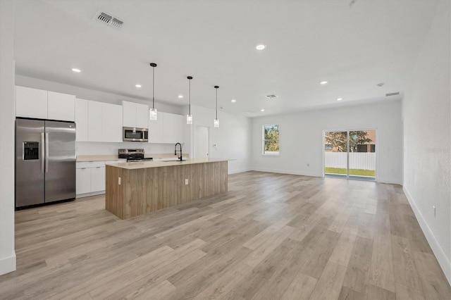 kitchen with white cabinets, an island with sink, appliances with stainless steel finishes, light wood-type flooring, and sink