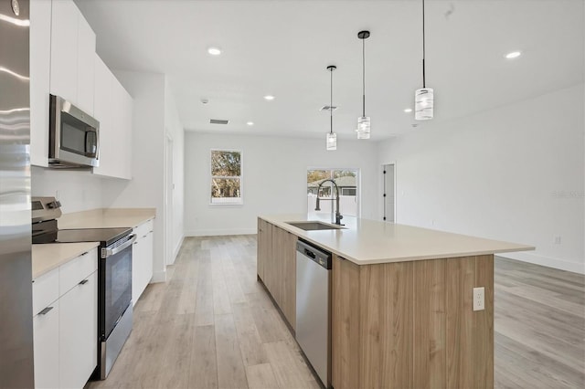 kitchen featuring light hardwood / wood-style floors, stainless steel appliances, a center island with sink, and white cabinets