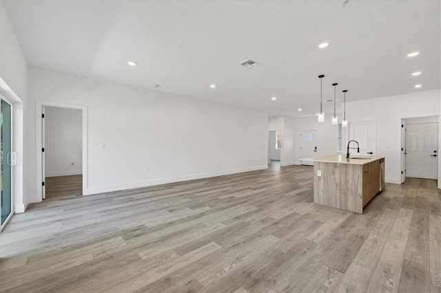 kitchen featuring sink, an island with sink, hanging light fixtures, light hardwood / wood-style floors, and light brown cabinets