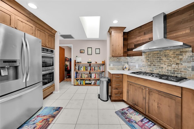 kitchen featuring wall chimney exhaust hood, tasteful backsplash, stainless steel appliances, and light tile patterned floors