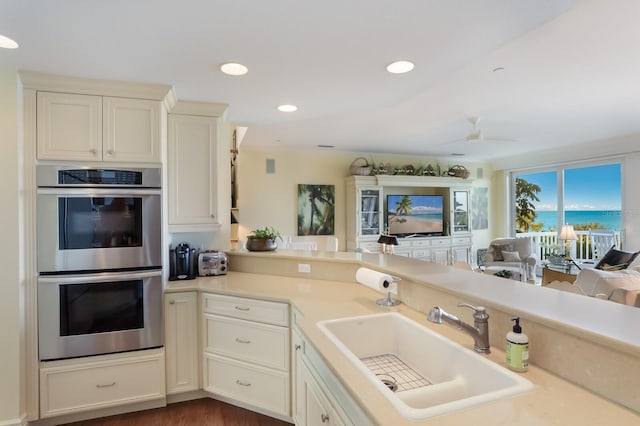 kitchen with double oven, ceiling fan, sink, and kitchen peninsula