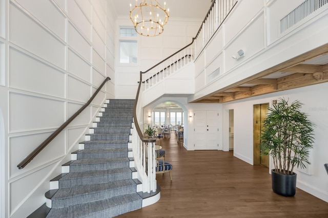 stairway with hardwood / wood-style floors, an inviting chandelier, crown molding, and a towering ceiling