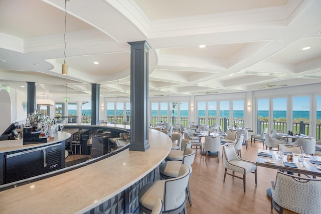 interior space featuring hardwood / wood-style flooring, a water view, decorative columns, and coffered ceiling