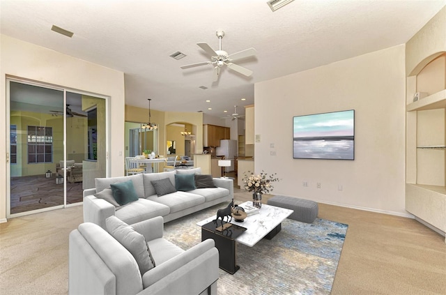 carpeted living room featuring a textured ceiling and ceiling fan with notable chandelier