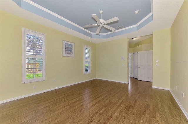 empty room featuring hardwood / wood-style floors, ceiling fan, crown molding, and a raised ceiling