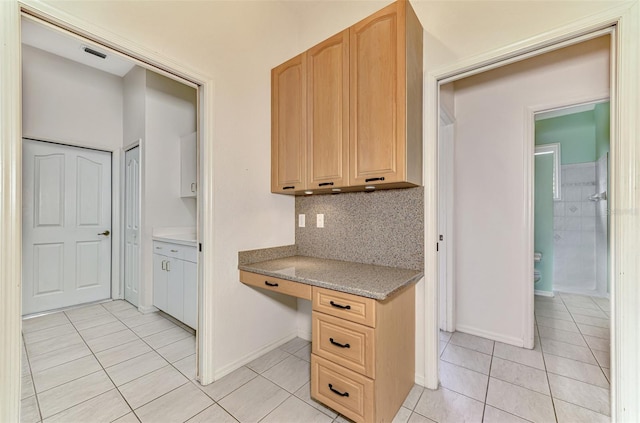 kitchen with light brown cabinets, decorative backsplash, built in desk, and light tile patterned floors