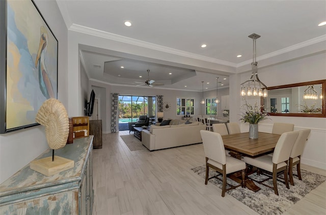 dining space featuring ornamental molding, a tray ceiling, ceiling fan with notable chandelier, and light wood-type flooring