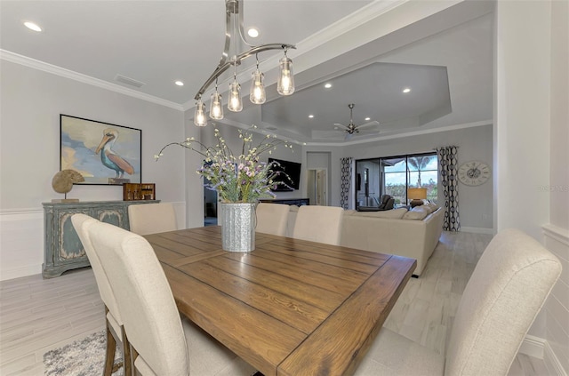 dining space with light hardwood / wood-style floors, a raised ceiling, ornamental molding, and ceiling fan